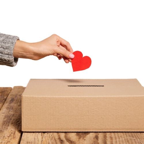 a hand putting a red heart into a donation box