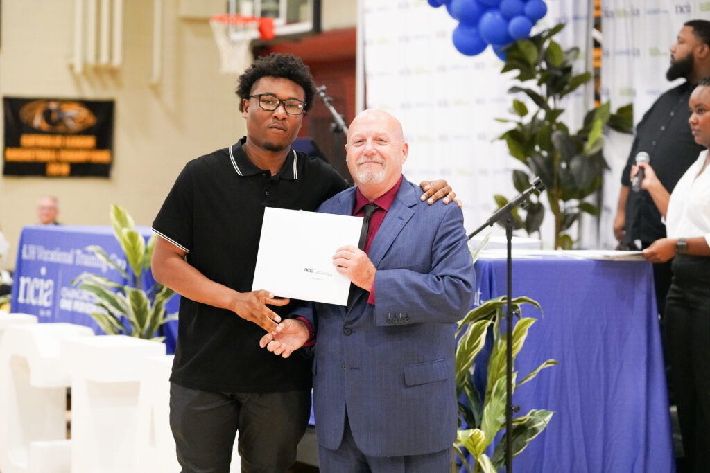 2 men standing at NCIA graduation, 1 holds a certificate