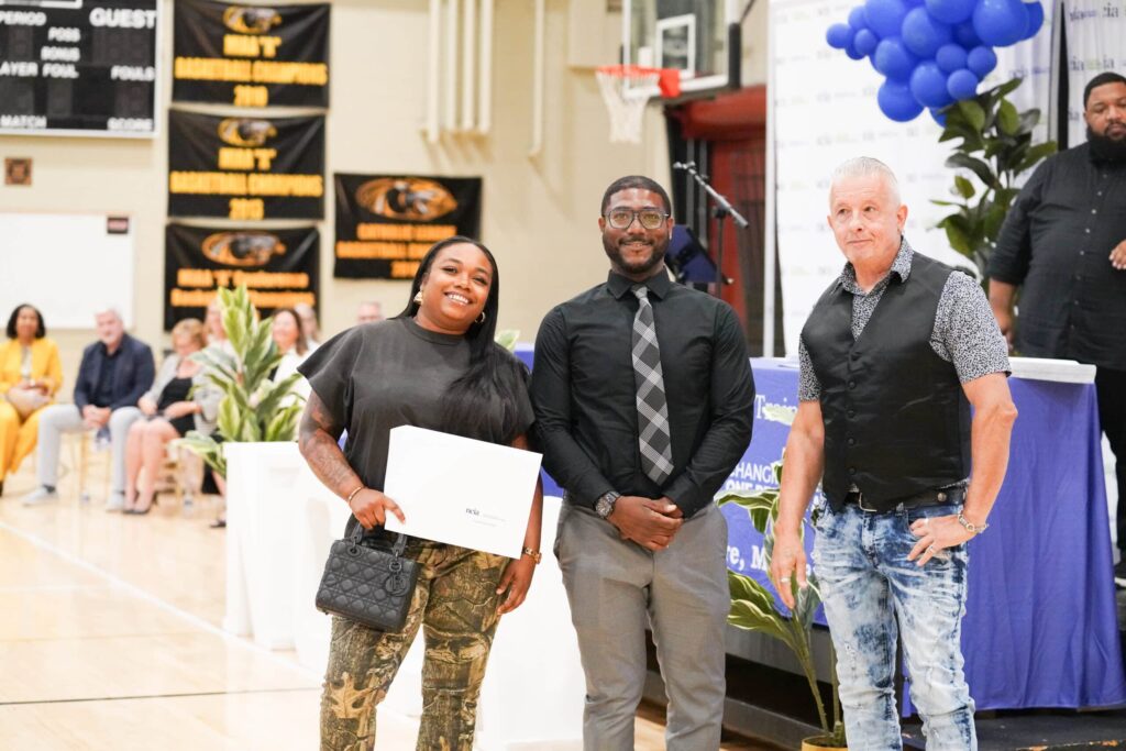 one woman and two men at graduation, the woman is holding her certificate