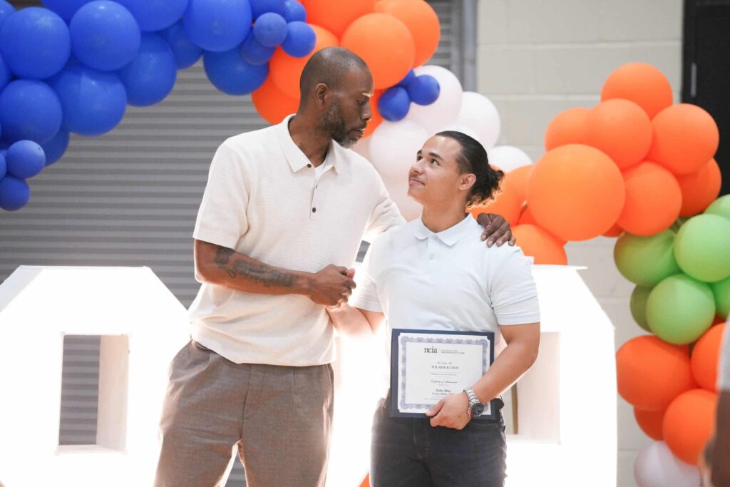 two people shaking hands, one with his ncia certification in hand